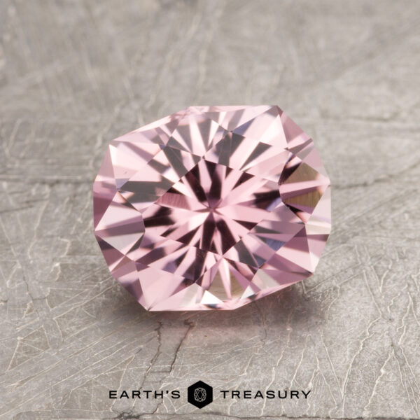 1.50-Carat Pink Tourmaline The ET1610, a pink gemstone with intricate facets, rests on a textured gray surface.