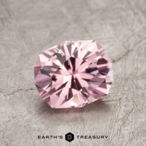 A faceted ET1620 pink gemstone rests on a textured gray surface.