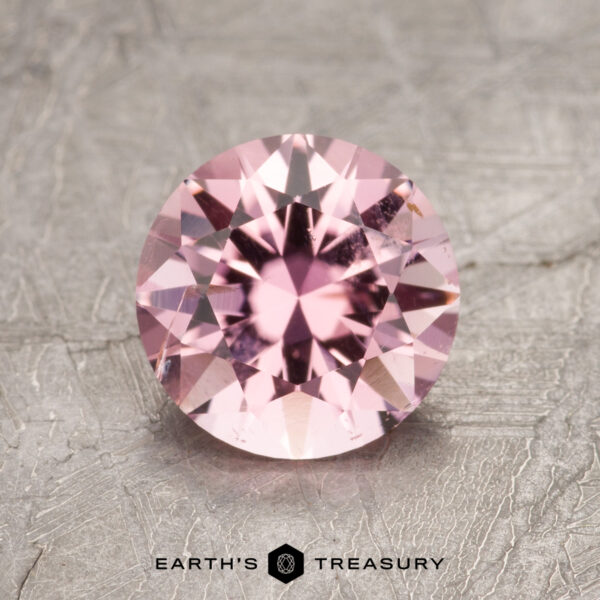 1.34-Carat Pink Tourmaline ET1635 gemstone resting on a textured gray surface with the "Earth's Treasury" logo.