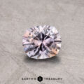 A 0.90-carat Montana Sapphire, with a pale pink and white hue, set against a textured gray background. It features an intricate cut pattern that enhances its reflective sparkle, with the "Earth's Treasury" logo visible beneath it.