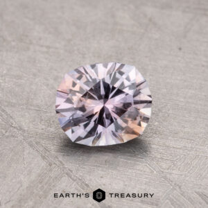 A 0.90-carat Montana Sapphire, with a pale pink and white hue, set against a textured gray background. It features an intricate cut pattern that enhances its reflective sparkle, with the "Earth's Treasury" logo visible beneath it.