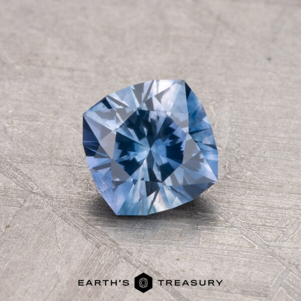 0.91-Carat Montana Sapphire (Heated) Displayed on a textured gray surface with the Earth's Treasury logo is a 0.91-carat, cushion-cut Montana sapphire gemstone.