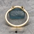 The "Fiona" band in 18k yellow gold stands upright in front of a textured blue stone, with a logo reading "Earth's Treasury" at the bottom.