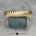 The "Damon" ring in 18k yellow gold, a twisted masterpiece, elegantly rests on a textured blue stone with "Earth's Treasury" subtly inscribed below.