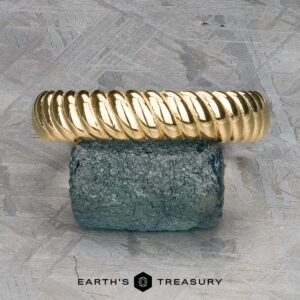 The "Damon" ring in 18k yellow gold, a twisted masterpiece, elegantly rests on a textured blue stone with "Earth's Treasury" subtly inscribed below.