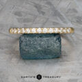 The "Lynn" band, a gold masterpiece in 18k yellow gold, is elegantly displayed on a blue gemstone against a textured gray background. At the bottom, sophisticated text reads "Earth's Treasury.