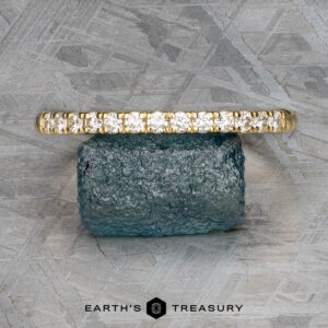 The "Lynn" band, a gold masterpiece in 18k yellow gold, is elegantly displayed on a blue gemstone against a textured gray background. At the bottom, sophisticated text reads "Earth's Treasury.