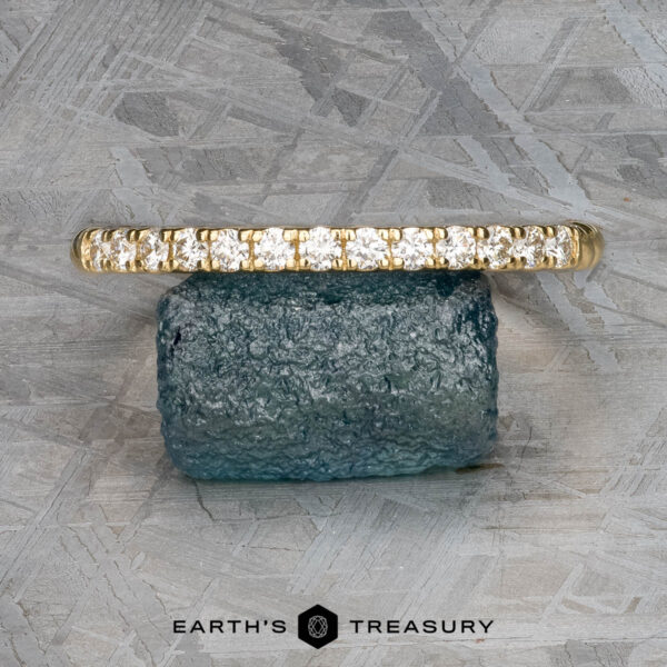 The "Lynn" band in 18k yellow gold The "Lynn" band, a gold masterpiece in 18k yellow gold, is elegantly displayed on a blue gemstone against a textured gray background. At the bottom, sophisticated text reads "Earth's Treasury.
