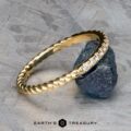 The Lynn band in 18k yellow gold showcases a twisted design adorned with small diamonds, elegantly resting on a rough stone.
