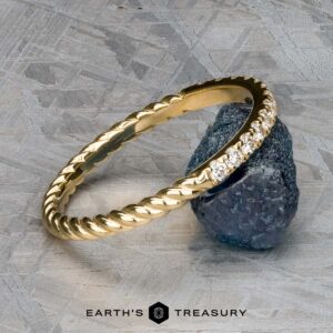 The Lynn band in 18k yellow gold showcases a twisted design adorned with small diamonds, elegantly resting on a rough stone.