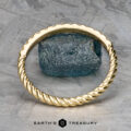 The "Lynn" band in 18k yellow gold features a twisted design and textured finish, artfully balanced on a rugged blue stone with a metallic background. Text reads "Earth's Treasury.