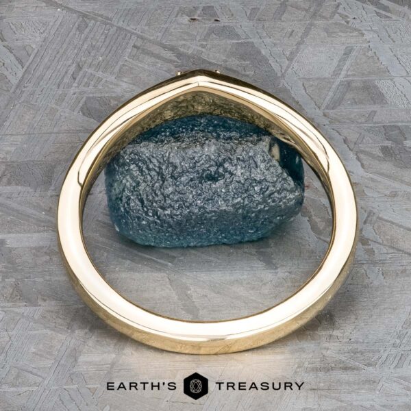 The "Zinnia" band in 14k yellow gold with orange sapphire The "Zinnia" band in 14k yellow gold stands upright, framing an orange sapphire on a textured gray surface. The “Earth’s Treasury” logo appears at the bottom.