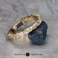 The "Mosaic" band in 14k yellow gold is displayed balanced on a rough dark stone, with the Earth’s Treasury logo at the bottom on a textured grey surface.