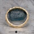 The "Mosaic" band in 14k yellow gold encircles a rough, dark green stone, displayed on a gray patterned surface with "Earth's Treasury" branding below.
