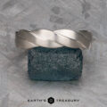 A platinum "Conall" ring stands upright on a rough blue gemstone, set against a textured gray background with the text "EARTH'S TREASURY" displayed below.