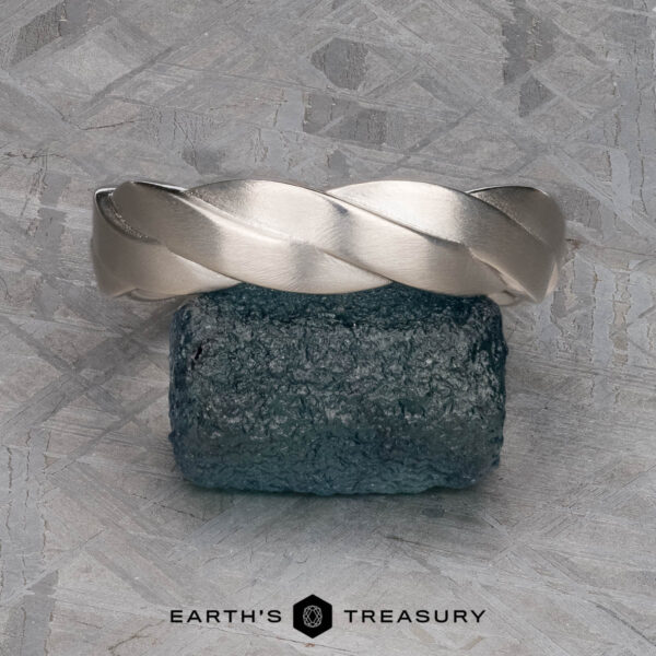 The "Conall" ring in platinum A platinum "Conall" ring stands upright on a rough blue gemstone, set against a textured gray background with the text "EARTH'S TREASURY" displayed below.