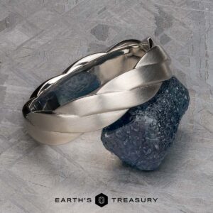 A platinum Conall ring rests on a rough dark blue gemstone, with the text "Earth's Treasury" at the bottom of the image.