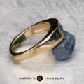 The "Milan" ring in 14k yellow gold with a 1.03-carat Montana sapphire rests on a green and white surface, with The Earth's Treasury logo visible at the bottom.