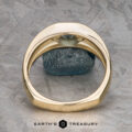 The "Milan" ring in 14k yellow gold with a 1.03-carat Montana sapphire stands upright before a gray stone on a textured surface, with the "Earth's Treasury" logo displayed at the bottom.