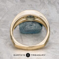 The "Milan" ring in 14k yellow gold with a 1.03-carat Montana sapphire rests on a green and white surface, with The Earth's Treasury logo visible at the bottom.