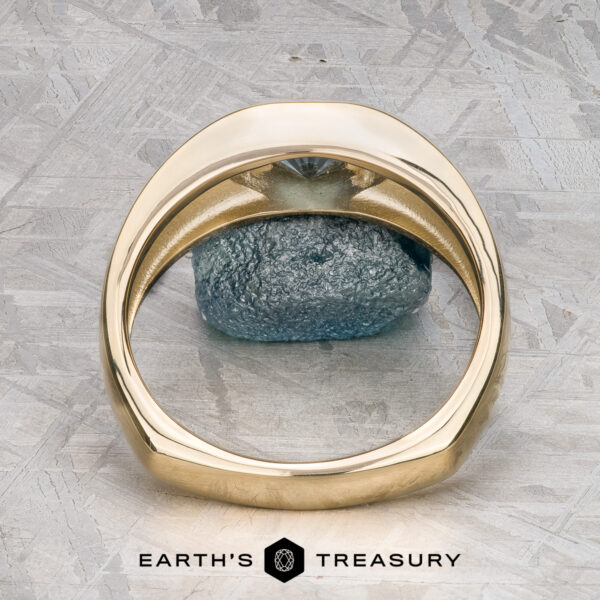 The "Milan" ring in 14k yellow gold with 1.03-carat Montana sapphire The "Milan" ring in 14k yellow gold with a 1.03-carat Montana sapphire rests on a green and white surface, with The Earth's Treasury logo visible at the bottom.