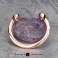 A rough purple gemstone set in the Jetty band in 14k rose gold rests on a textured gray surface, with the "Earth's Treasury" logo below.