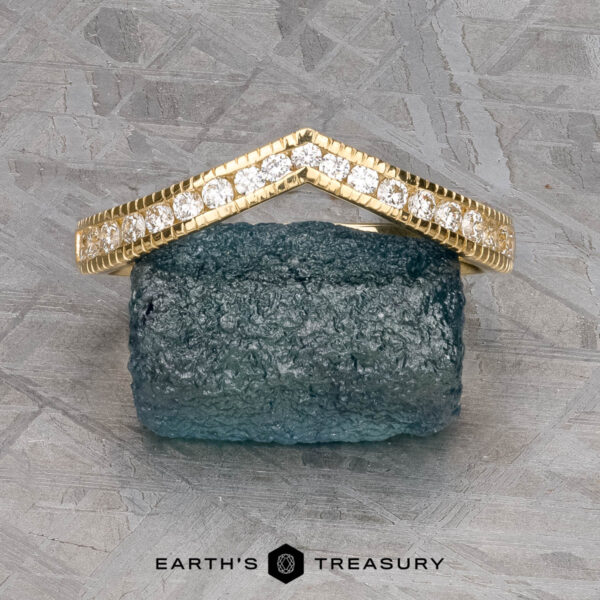 The "Ramona" band in 18k yellow gold The "Ramona" band in 18k yellow gold, set with small diamonds, is shown resting on a rough blue gemstone with "Earth's Treasury" branding below.