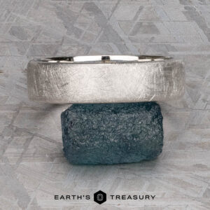 The "Madeira" ring in platinum rests on a rough blue stone, set against a textured gray background with the text "EARTH'S TREASURY" below.