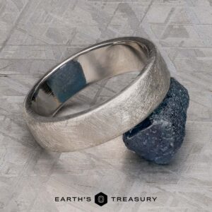 The "Madeira" ring in platinum rests on a rough, dark stone atop a textured metallic surface, with "EARTH'S TREASURY" displayed at the bottom.