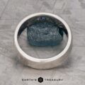 The "Madeira" ring in platinum with a small blue gemstone is displayed upright on a textured gray surface, the Earth's Treasury logo positioned below.