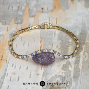 The "Analise" Yogo Sapphire and Diamond Tennis Bracelet in 14k yellow gold is displayed on a light, textured background with the "Earth's Treasury" logo visible at the bottom.