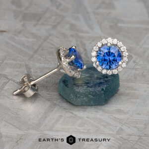 A stunning set of halo earrings, crafted with blue sapphires encircled by dazzling diamonds, is showcased on a textured surface, with "Stacked from 16 images. Method=B (R=1,S=3)" elegantly inscribed at the bottom.