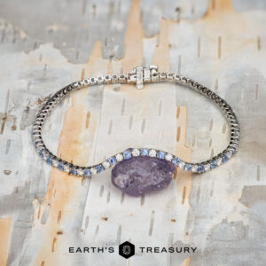 The "Analise" Yogo Sapphire and Diamond Tennis Bracelet in 14k white gold is shown on a textured, multicolored background. "Earth's Treasury" appears at the bottom.