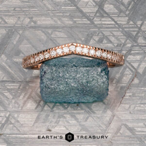The "Ramona" band in 14K rose gold rests on a rough blue stone atop a geometric silver background, with the “Earth's Treasury” logo displayed below.