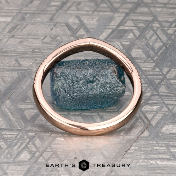 The "Ramona" band in 14K rose gold The "Ramona" band in 14K rose gold rests on a rough blue stone atop a geometric silver background, with the “Earth's Treasury” logo displayed below.