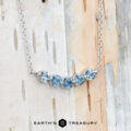 The "Breeze" Necklace in 14K white gold, featuring five round blue gemstones, is displayed against a light-textured background with the Earth’s Treasury logo at the bottom.