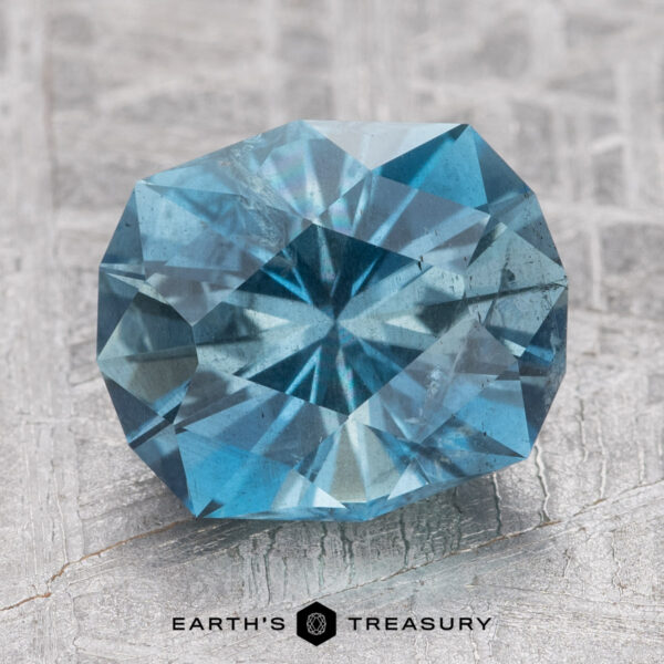 2.84-Carat Nasarawa Teal Aqua A round, faceted teal Aqua gemstone is placed on a textured surface, with the text "Earth's Treasury" below it.