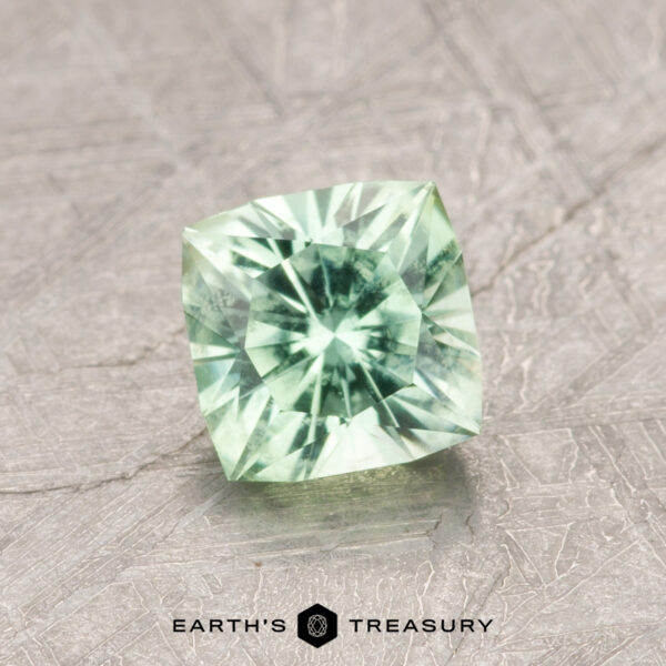 0.91-Carat Bright Green Kornerupine A green cushion-cut gemstone labeled as ET1171 is displayed on a textured surface, with the words "Earth's Treasury" visible below.