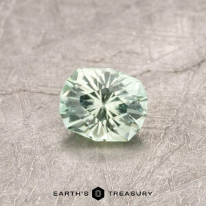 The ET1181 gemstone, a faceted light green stone, is showcased on a textured grey surface with the words "Earth's Treasury" at the bottom.