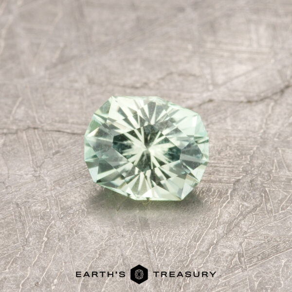 0.51-Carat Bright Mint Green Kornerupine The ET1181 gemstone, a faceted light green stone, is showcased on a textured grey surface with the words "Earth's Treasury" at the bottom.