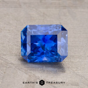 A vivid 1.65-carat rectangular, faceted Ceylon Sapphire sparkles brilliantly on a textured surface, its depth enhanced through expert heating.