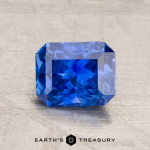 A vivid 1.65-carat rectangular, faceted Ceylon Sapphire sparkles brilliantly on a textured surface, its depth enhanced through expert heating.