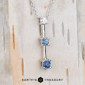 The "Dusk" Necklace in 14k white gold features a chain with three round gemstones—one white, two blue—set vertically, hanging gracefully against a light, textured background.