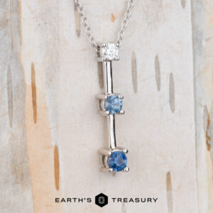 The "Dusk" Necklace in 14k white gold features a chain with three round gemstones—one white, two blue—set vertically, hanging gracefully against a light, textured background.