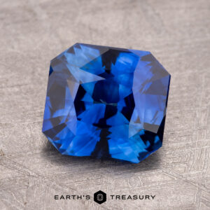 A vibrant Sky Blue Ceylon Sapphire, featuring triangular facets, dazzles on a textured gray surface. The 2.59-carat gemstone has been masterfully heated, enhancing its brilliant hue and charm.