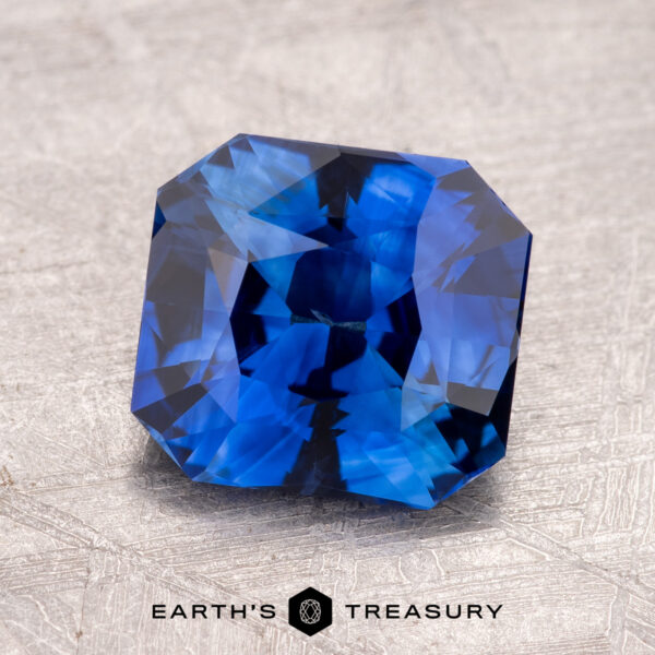 A vibrant Sky Blue Ceylon Sapphire, featuring triangular facets, dazzles on a textured gray surface. The 2.59-carat gemstone has been masterfully heated, enhancing its brilliant hue and charm.