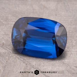 A rectangular sky blue 3.29-carat Ceylon sapphire, enhanced through heating, with faceted cuts is placed on a textured surface.