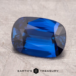 A rectangular sky blue 3.29-carat Ceylon sapphire, enhanced through heating, with faceted cuts is placed on a textured surface.