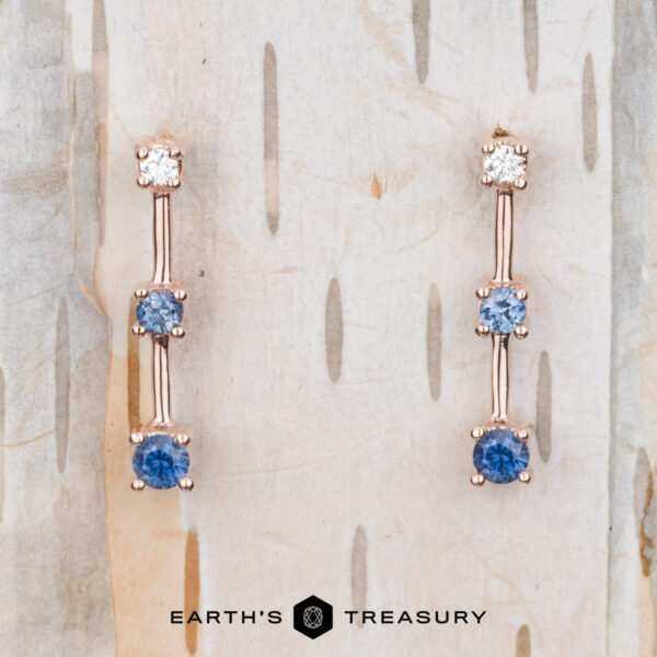 The "Dusk" Earrings in 14k rose gold Introducing the exquisite "Dusk" Earrings in 14k rose gold: drop earrings adorned with alternating white and blue gemstones on a textured background. These stunning pieces of jewelry capture the essence of elegance and are perfect for any occasion.