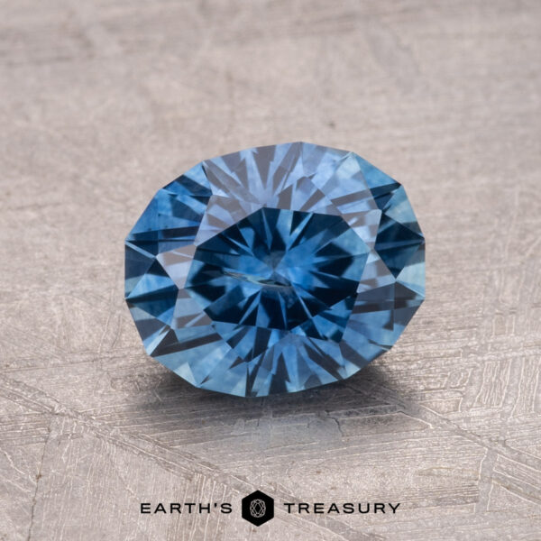 1.82-Carat Montana Sapphire (Heated) A 1.82-carat Montana sapphire (heated) gemstone rests on a textured gray surface, showcasing its faceted cut and reflecting light.
